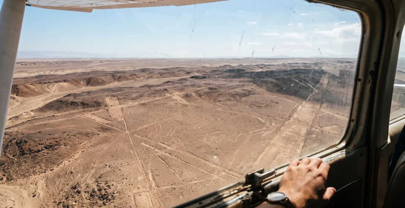 Vue aérienne depuis la hublot d'un petit avion survolant le désert de Nazca, où des lignes géoglyphiques apparaissent sur le sol aride.